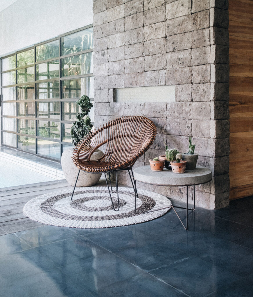 Nature-inspired patio seating with wicker chair, potted plants, and rustic stone wall – sustainable interior design aesthetic"